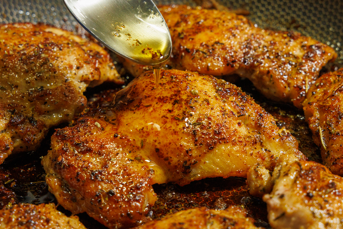 Melted butter dripping from a spoon onto a chicken thigh.